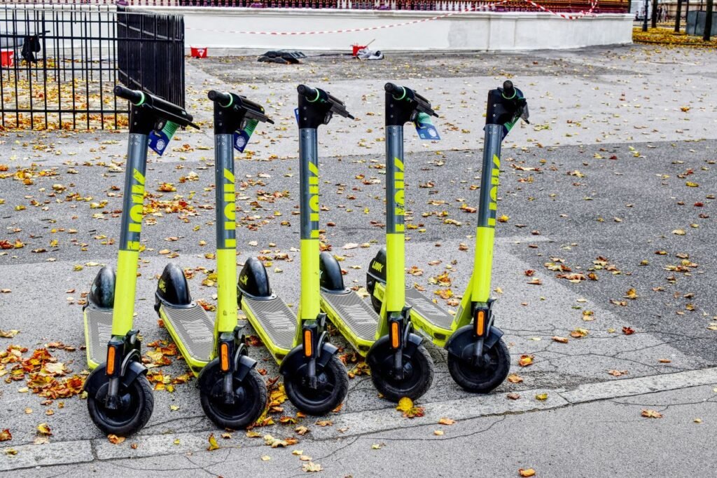 Find Your Perfect Match Five lime green e-scooters parked in a row on a leaf-strewn street during autumn.