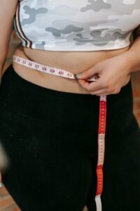 Crop anonymous plus size female in sportswear measuring big belly with measuring tape